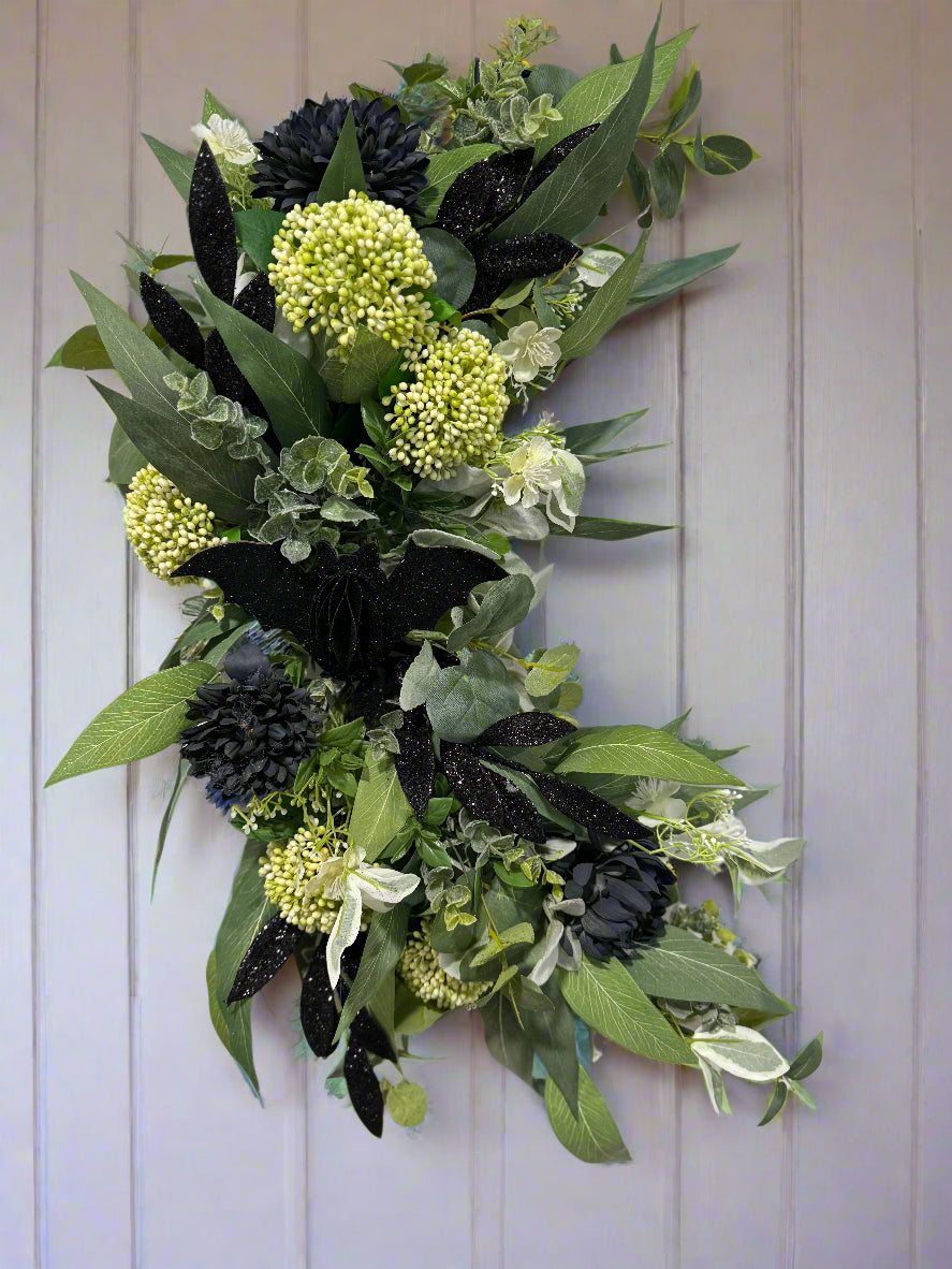 Decorative crescent shaped wreath with green foliage and glittery black halloween elements