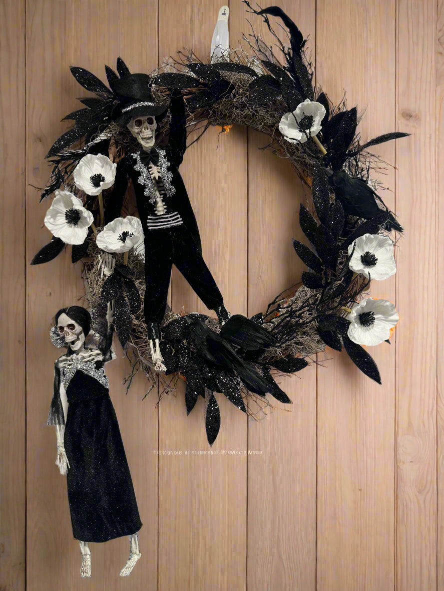 Halloween wreath with skeletons, black and white flowers on a plain wall.