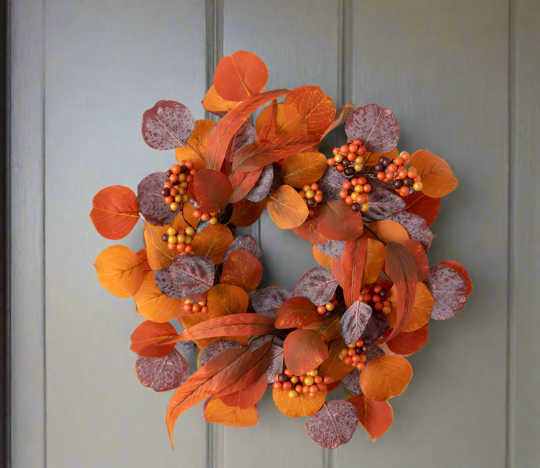 A fall-themed wreath decoration featuring a circle of artificial berry clusters and twisted eucalyptus branches in shades of orange, brown, and purple.