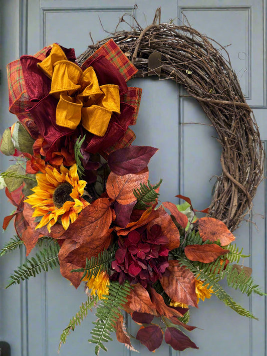 Autumn-themed wreath with leaves and flowers and a luxurious bow