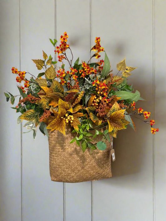 Decorative wall basket with autumn-themed flowers and leaves on a light wooden panel background