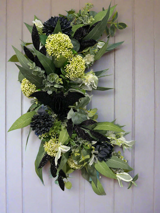 Decorative crescent shaped wreath with green foliage and glittery black halloween elements 