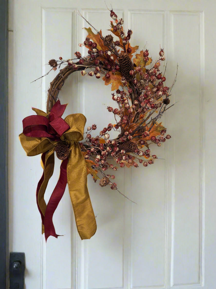 Decorative wreath with autumnal elements such as berries, leaves and pinecones with a dramatic bow 